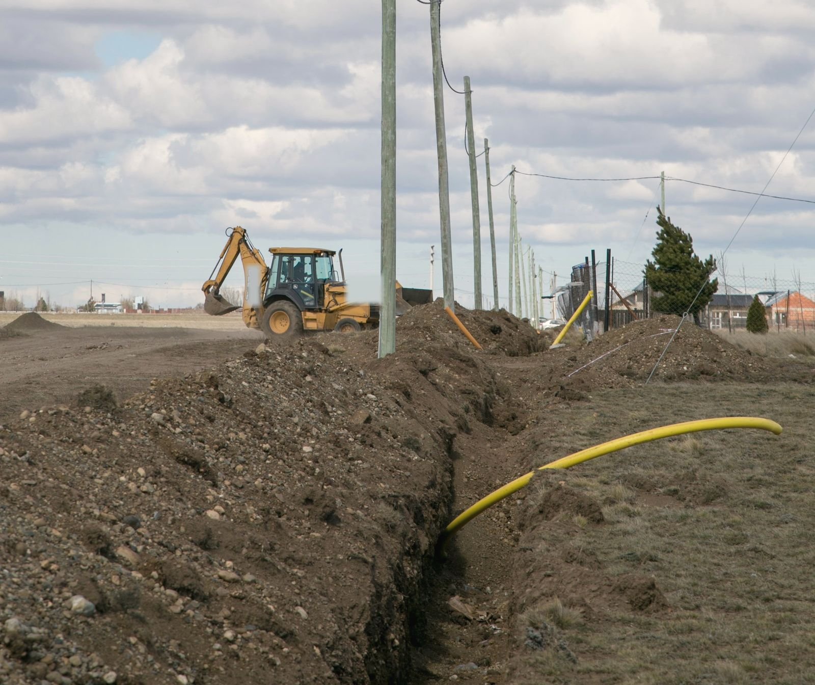 Backhoe cutting a utility trench beside a row of poles