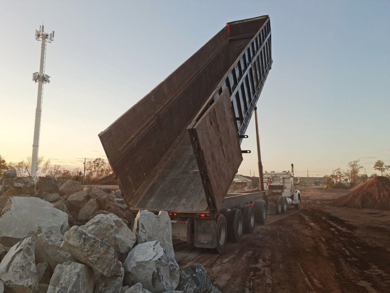 Dump trailer raised at a job site at dusk